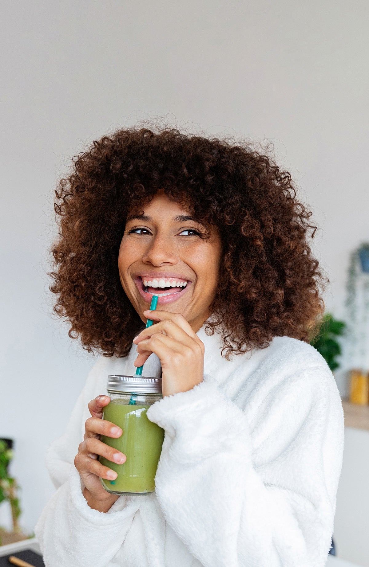 Woman holding a green smoothie with a straw, wearing a white sweater.